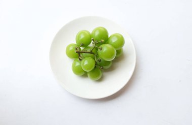 Beyaz arka planda izole edilmiş beyaz bir tabağa yerleştirilmiş güzel bir misket üzümü demeti.