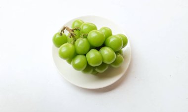 Beyaz arka planda izole edilmiş beyaz bir tabağa yerleştirilmiş güzel bir misket üzümü demeti.
