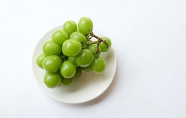 Beyaz arka planda izole edilmiş beyaz bir tabağa yerleştirilmiş güzel bir misket üzümü demeti.
