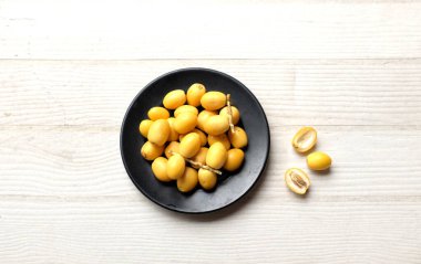 Taze palmiye anka kuşu dactylifera ya da halka tabakta hurma meyvesi, beyaz ahşap bir zeminde siyah seramik