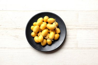 Taze palmiye anka kuşu dactylifera ya da halka tabakta hurma meyvesi, beyaz ahşap bir zeminde siyah seramik