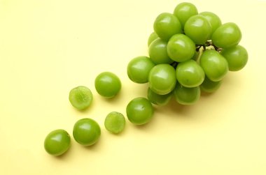 Bir demet taze tatlı yeşil muscat (Vitis vinifera) üzümü sarı arka fonda izole edilmiş. Yeşil üzümler. Japon üzümleri. Üzüm yeşili. Tadı tatlı ve doğal..