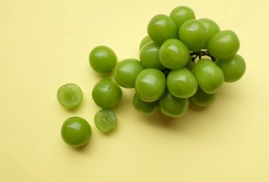 Bir demet taze tatlı yeşil muscat (Vitis vinifera) üzümü sarı arka fonda izole edilmiş. Yeşil üzümler. Japon üzümleri. Üzüm yeşili. Tadı tatlı ve doğal..