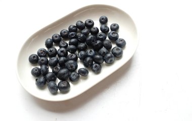 Taze organik sulu yaban mersini, olgun tatlı yaban mersini beyaz bir oval seramik kapta beyaz bir arkaplanda izole edilmiş. Yabanmersini arka planı. Metnin için kopyalama alanı ile. Vejetaryen ve vejetaryen Sağlık