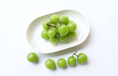 Beyaz bir sırt damlasında beyaz oval seramik tabakta izole edilmiş taze, tatlı yeşil Muscat (Vitis vinifera) üzümü. Japon üzümleri. Üzüm yeşili. Tadı tatlı ve doğal..