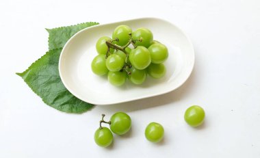 Beyaz bir sırt damlasında beyaz oval seramik tabakta izole edilmiş taze, tatlı yeşil Muscat (Vitis vinifera) üzümü. Japon üzümleri. Üzüm yeşili. Tadı tatlı ve doğal..