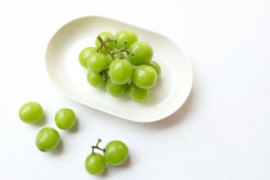 Beyaz bir sırt damlasında beyaz oval seramik tabakta izole edilmiş taze, tatlı yeşil Muscat (Vitis vinifera) üzümü. Japon üzümleri. Üzüm yeşili. Tadı tatlı ve doğal..