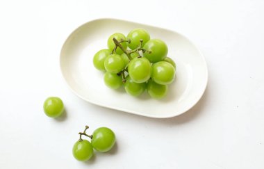 Beyaz bir sırt damlasında beyaz oval seramik tabakta izole edilmiş taze, tatlı yeşil Muscat (Vitis vinifera) üzümü. Japon üzümleri. Üzüm yeşili. Tadı tatlı ve doğal..