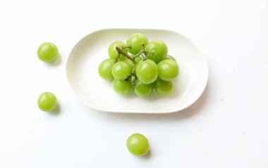 Beyaz bir sırt damlasında beyaz oval seramik tabakta izole edilmiş taze, tatlı yeşil Muscat (Vitis vinifera) üzümü. Japon üzümleri. Üzüm yeşili. Tadı tatlı ve doğal..