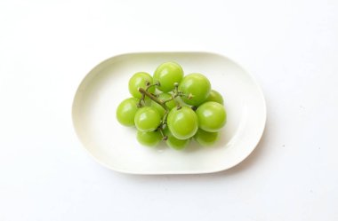 Beyaz bir sırt damlasında beyaz oval seramik tabakta izole edilmiş taze, tatlı yeşil Muscat (Vitis vinifera) üzümü. Japon üzümleri. Üzüm yeşili. Tadı tatlı ve doğal..