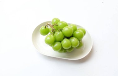 Beyaz bir sırt damlasında beyaz oval seramik tabakta izole edilmiş taze, tatlı yeşil Muscat (Vitis vinifera) üzümü. Japon üzümleri. Üzüm yeşili. Tadı tatlı ve doğal..
