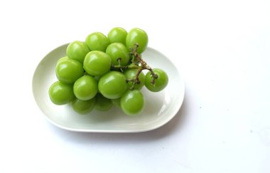 Beyaz bir sırt damlasında beyaz oval seramik tabakta izole edilmiş taze, tatlı yeşil Muscat (Vitis vinifera) üzümü. Japon üzümleri. Üzüm yeşili. Tadı tatlı ve doğal..