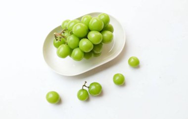 Beyaz bir sırt damlasında beyaz oval seramik tabakta izole edilmiş taze, tatlı yeşil Muscat (Vitis vinifera) üzümü. Japon üzümleri. Üzüm yeşili. Tadı tatlı ve doğal..
