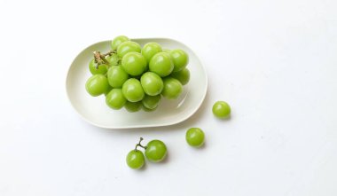Beyaz bir sırt damlasında beyaz oval seramik tabakta izole edilmiş taze, tatlı yeşil Muscat (Vitis vinifera) üzümü. Japon üzümleri. Üzüm yeşili. Tadı tatlı ve doğal..