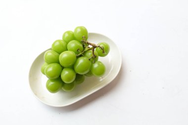 Beyaz bir sırt damlasında beyaz oval seramik tabakta izole edilmiş taze, tatlı yeşil Muscat (Vitis vinifera) üzümü. Japon üzümleri. Üzüm yeşili. Tadı tatlı ve doğal..