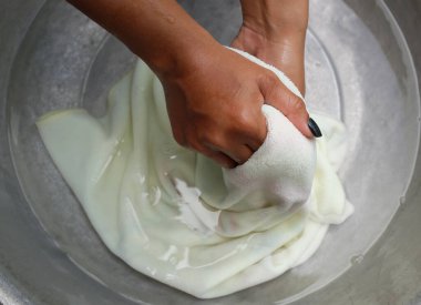 Asyalı ev hanımı, alüminyum leğende renkli beyaz havluları köpüklü deterjanla yıkıyor. Üst manzara. Çamaşır konsepti..