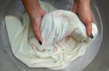 Asyalı ev hanımı, alüminyum leğende renkli beyaz havluları köpüklü deterjanla yıkıyor. Üst manzara. Çamaşır konsepti..