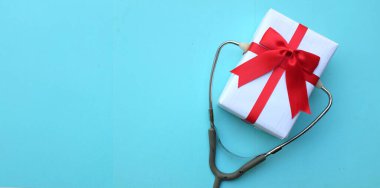 Mavi pastel arka planda izole edilmiş hediye kutusu olan tıbbi steteskop. konsept noel ve yeni yıl. Yatay fotoğraf