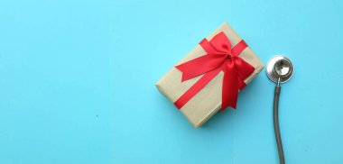 Mavi pastel arka planda izole edilmiş hediye kutusu olan tıbbi steteskop. konsept noel ve yeni yıl. Yatay fotoğraf
