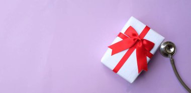Mor renkli arka planda izole edilmiş hediye kutusu olan tıbbi steteskop. konsept noel ve yeni yıl. Yatay fotoğraf