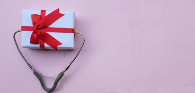 Pembe pastel arka planda izole edilmiş hediye kutusu olan tıbbi steteskop. konsept noel ve yeni yıl. Yatay fotoğraf