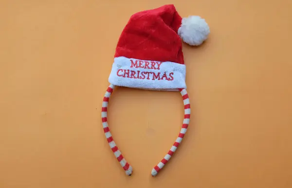 Beautiful headband  Decorative red Santa Hat isolate on a orange backdrop.concept of joyful Christmas party,New year is coming soon, festive season decoration with Christmas elements