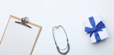 Üst ve düz, uzay doktorlarının ofis masasının fotokopisi. Tıbbi aksesuarlar, boş tıbbi pano, steteskop ve mavi kurdeleli el işi kağıt kutu, gözlük, beyaz perde arkasında kalem izolasyonu.