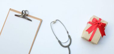 Üst ve düz, uzay doktorlarının ofis masasının fotokopisi. Tıbbi aksesuarlar, boş tıbbi pano, steteskop ve el işi kağıt kutu içinde kırmızı kurdele, gözlük, beyaz perde arkasında kalem izolasyonu.