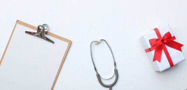 Üst ve düz, uzay doktorlarının ofis masasının fotokopisi. Tıbbi aksesuarlar, boş tıbbi pano, steteskop ve el işi kağıt kutu içinde kırmızı kurdele, gözlük, beyaz perde arkasında kalem izolasyonu.