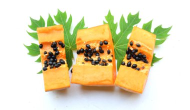 Üst ve düz bir zemin üzerinde yeşil yapraklı, dilimlenmiş, olgun bir papaya meyvesi papaya uzanır. Sağlıklı beslenme için sebze ve meyve.