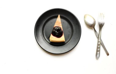 Üst ve düz katmanlı yaban mersinli kekin bir kısmı siyah bir tabakta mor yaban mersinli ve beyaz bir arkaplanda yaban mersinli.