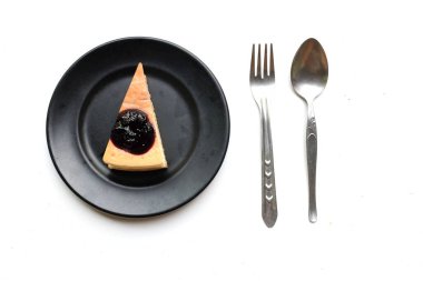 Üst ve düz katmanlı yaban mersinli kekin bir kısmı siyah bir tabakta mor yaban mersinli ve beyaz bir arkaplanda yaban mersinli.