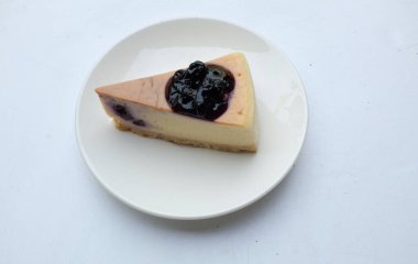 Üst ve düz bir porsiyon yaban mersinli kek beyaz bir plaka üzerinde mor yaban mersinli süsleme beyaz zemin üzerinde izole