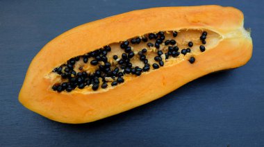 Üst ve düz bir zemin üzerinde yeşil yapraklı, dilimlenmiş, olgun bir papaya meyvesi papaya uzanır. Sağlıklı beslenme için sebze ve meyve.