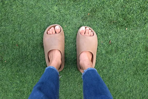 female legs in a pair of slides with an open toe pillow isolated on the green grass background. women's fashion. women's summer footwear,soft slippers.A women wearing jeans with sandals