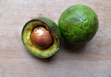  Taze çiğ avokado (Persea americana) bütün yeşil yapraklı meyve, yarısı dilimlenmiş, ahşap masa arkası üzerinde izole edilmiş. Meyve ve ve ve ve sağlıklı yiyecek, vejetaryen gıda, kilo kaybı, beyin sağlığı