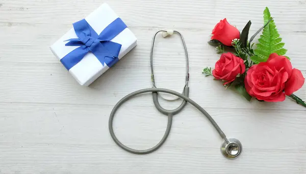 Top view and copy space gift box, bouquet of red roses, stethoscope Red hearts, isolate on a wooden table white backdrop, Valentines Day concept. World Health Day, Doctors Day, Nurses Day