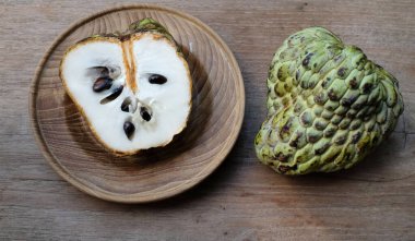 Taze yeşil kremalı elma, elma şekeri, annona cherimola (annona squamosa l..), ahşap bir masada izole edilmiş bir tabakta ikiye bölünmüş meyve. Tropikal egzotik meyve ve sağlıklı meyve