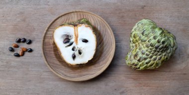 Taze yeşil kremalı elma, elma şekeri, annona cherimola (annona squamosa l..), ahşap bir masada izole edilmiş bir tabakta ikiye bölünmüş meyve. Tropikal egzotik meyve ve sağlıklı meyve