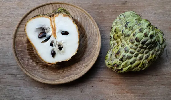 Taze yeşil kremalı elma, elma şekeri, annona cherimola (annona squamosa l..), ahşap bir masada izole edilmiş bir tabakta ikiye bölünmüş meyve. Tropikal egzotik meyve ve sağlıklı meyve