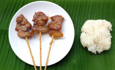 Tayland usulü domuz ızgara çubuğu ya da bambu çubuğuyla möö ping, yeşil muz yaprağından izole edilmiş seramik bir tabakta yapışkan pirinç. Geleneksel Tayland kahvaltısı.