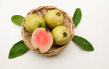 tatlı olgun pembe guava, kırmızı guava (psidyum guajava) yeşil yapraklı ve yarım dilimli meyve, sepetin içinde beyaz arka planda izole edilmiş, üst görünümde, düz yerde, sağlıklı meyve kavramı