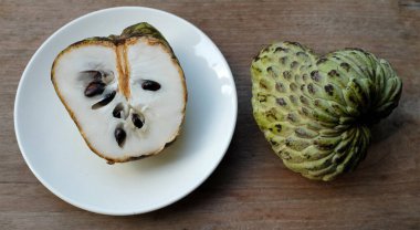 Taze yeşil kremalı elma, elma şekeri, annona cherimola (annona squamosa l..), tahta masa arkasında beyaz bir tabakta yapraklarla ikiye bölünmüş meyve. Tropikal egzotik meyve ve sağlık