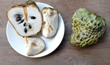 Taze yeşil kremalı elma, elma şekeri, annona cherimola (annona squamosa l..), tahta masa arkasında beyaz bir tabakta yapraklarla ikiye bölünmüş meyve. Tropikal egzotik meyve ve sağlık