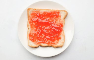 Ahududu çileği reçelinin kuş bakışı görüntüsü beyaz bir arkaplanda izole edilmiş seramik tabakta bir dilim ekmeğin üzerine serpiştirilmiş taze kırmızı böğürtlenler. Sağlıklı atıştırmalıklar ve yemek fikirleri