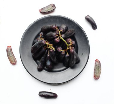 Olgun, çekirdeksiz Ay damlaları Üzüm, Parmak Üzümü, Cadı Parmak Üzümü, Sulu hamurlu safir üzümler Ahşap bir masa arkasında izole edilmiş siyah seramik bir tabakta yeşil yapraklar.