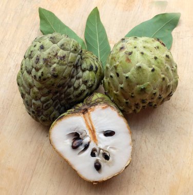 Taze yeşil kremalı elma, elma şekeri, annona cherimola (annona squamosa l.), tahta kesim tahtası arka planında yapraklarla ikiye bölünmüş meyve. Tropikal egzotik meyve ve sağlık