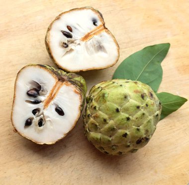 Taze yeşil kremalı elma, elma şekeri, annona cherimola (annona squamosa l.), tahta kesim tahtası arka planında yapraklarla ikiye bölünmüş meyve. Tropikal egzotik meyve ve sağlık