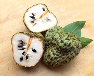 Taze yeşil kremalı elma, elma şekeri, annona cherimola (annona squamosa l.), tahta kesim tahtası arka planında yapraklarla ikiye bölünmüş meyve. Tropikal egzotik meyve ve sağlık