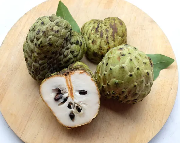 stock image fresh green raw custard apple,sugar apple, annona cherimola (annona squamosa l.) fruit cut in half sliced with leaves on a wooden cutting board  backdrop. tropical exotic fruit and health